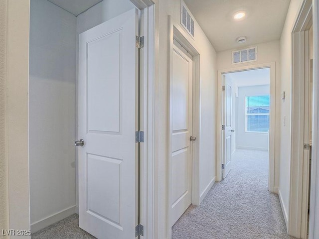 hall featuring visible vents, baseboards, and light colored carpet