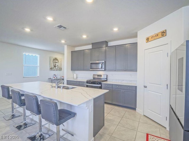 kitchen featuring visible vents, gray cabinets, a sink, appliances with stainless steel finishes, and a kitchen breakfast bar