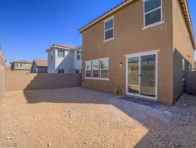 rear view of house with stucco siding, a fenced backyard, and a tiled roof