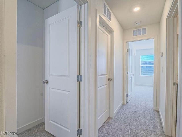 hallway featuring light carpet, visible vents, and baseboards