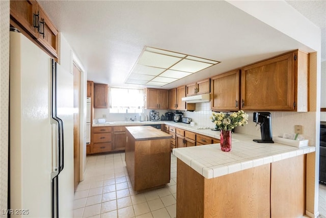 kitchen featuring white appliances, light tile patterned floors, decorative backsplash, light countertops, and under cabinet range hood