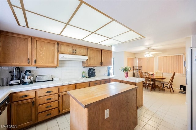 kitchen featuring under cabinet range hood, a peninsula, freestanding refrigerator, decorative backsplash, and dishwasher