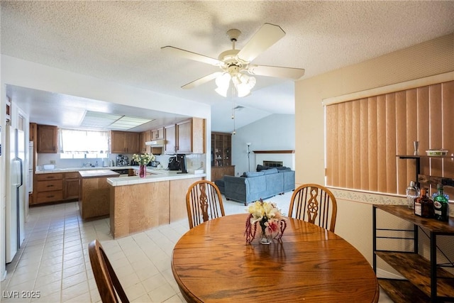 dining space with a fireplace, a ceiling fan, light tile patterned flooring, vaulted ceiling, and a textured ceiling