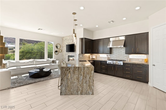 kitchen featuring visible vents, decorative backsplash, light stone counters, wall chimney range hood, and stainless steel gas cooktop