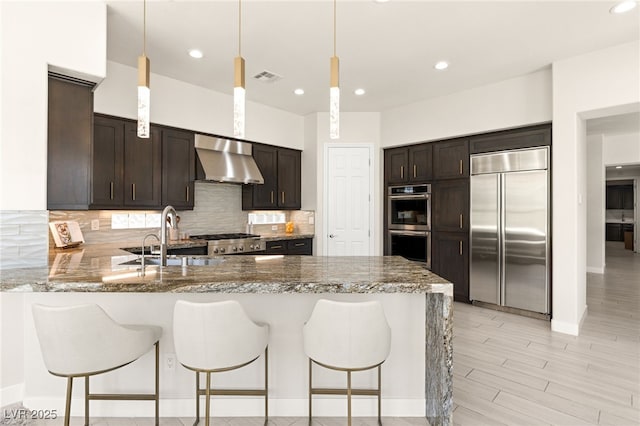 kitchen with stainless steel appliances, tasteful backsplash, visible vents, a peninsula, and wall chimney exhaust hood