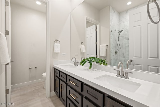 bathroom featuring a sink, a tile shower, toilet, and double vanity