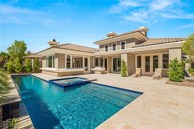 rear view of property with french doors, stucco siding, a pool with connected hot tub, a patio area, and a tiled roof