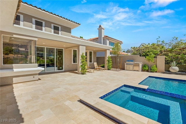 back of property featuring fence, exterior kitchen, a patio area, a pool with connected hot tub, and stucco siding