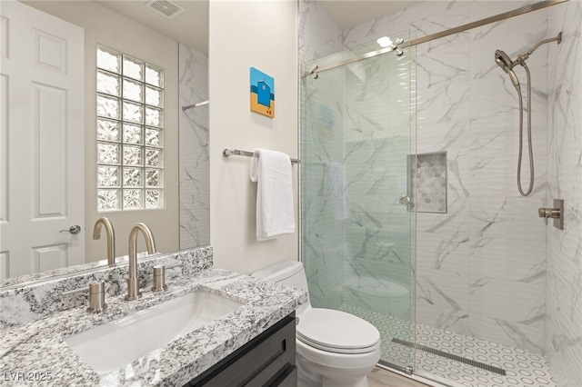 bathroom with a marble finish shower, visible vents, vanity, and toilet