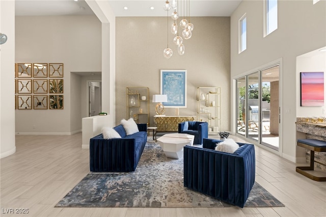 living area featuring a towering ceiling, a notable chandelier, baseboards, and wood finished floors