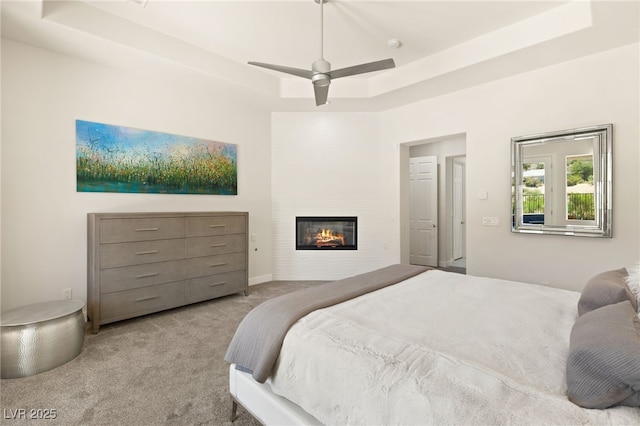 bedroom featuring a tray ceiling, carpet flooring, a fireplace, and ceiling fan