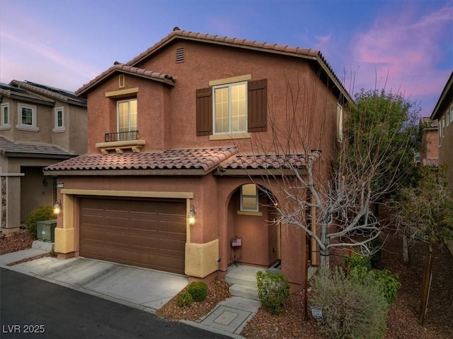 mediterranean / spanish home featuring a garage, a tiled roof, concrete driveway, and stucco siding