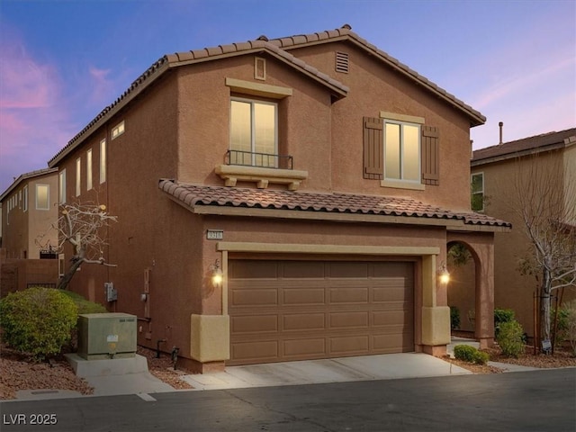 mediterranean / spanish house with a garage, driveway, a tiled roof, and stucco siding