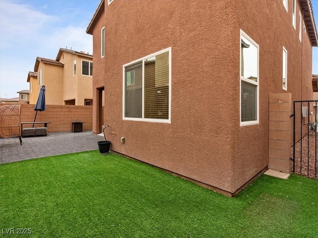 view of side of property featuring a yard, a patio area, fence, and stucco siding