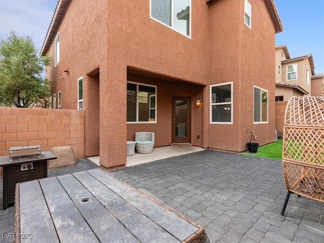 rear view of house with a patio area, fence, and stucco siding