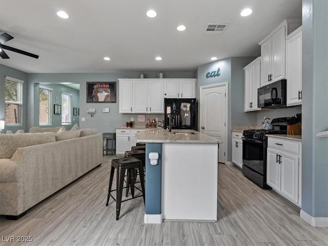 kitchen featuring a sink, visible vents, white cabinets, open floor plan, and black appliances