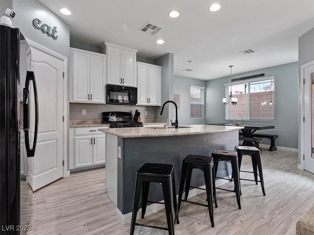 kitchen with visible vents, a breakfast bar area, black appliances, white cabinetry, and a sink