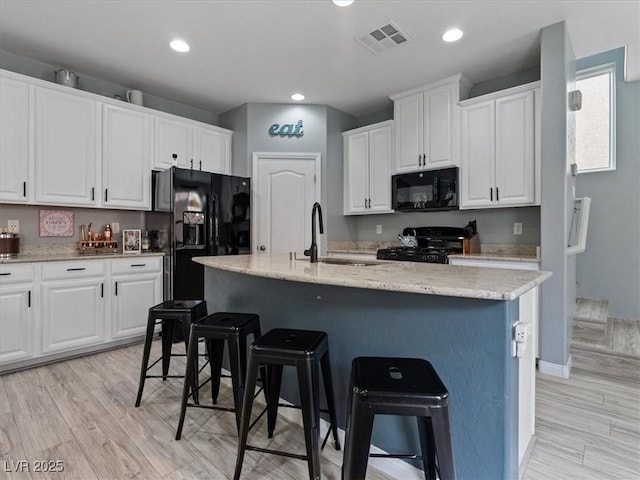 kitchen with white cabinets, black appliances, visible vents, and a kitchen breakfast bar