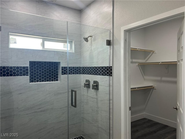 full bath with a stall shower, a spacious closet, baseboards, and wood finished floors
