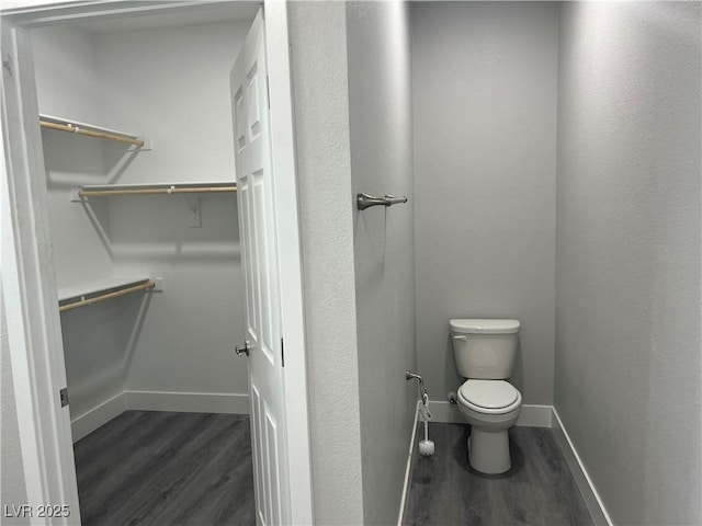 bathroom featuring a spacious closet, wood finished floors, toilet, and baseboards