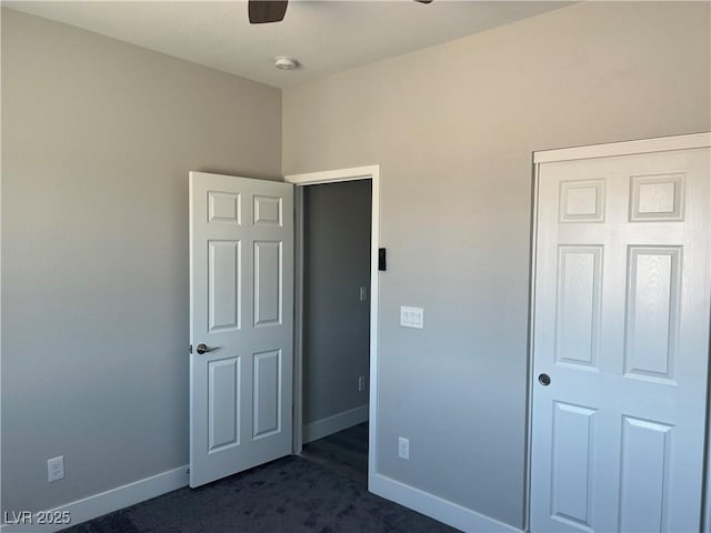 unfurnished bedroom featuring baseboards, dark carpet, ceiling fan, and a closet