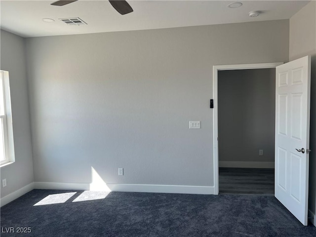 unfurnished room with dark colored carpet, visible vents, ceiling fan, and baseboards