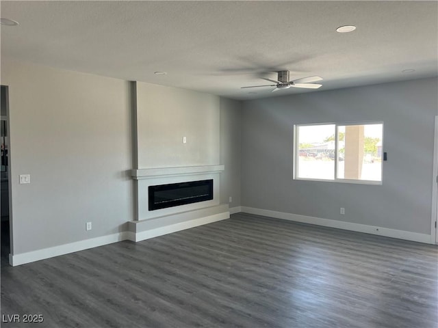 unfurnished living room with a textured ceiling, a ceiling fan, dark wood finished floors, baseboards, and a glass covered fireplace
