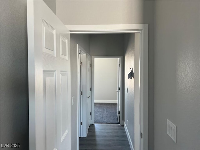 corridor with a textured wall, dark wood finished floors, and baseboards