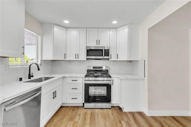 kitchen with appliances with stainless steel finishes, white cabinetry, a sink, and light wood finished floors