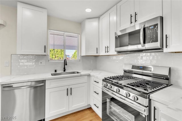 kitchen featuring appliances with stainless steel finishes, white cabinetry, a sink, and light stone countertops