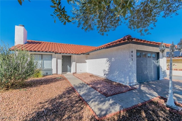 mediterranean / spanish house featuring a chimney, an attached garage, a tile roof, and stucco siding