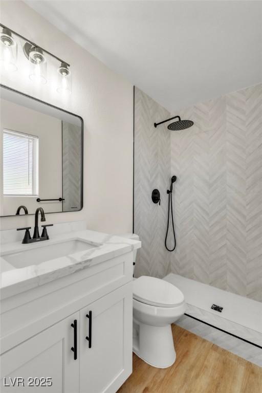 bathroom featuring toilet, wood finished floors, tiled shower, and vanity