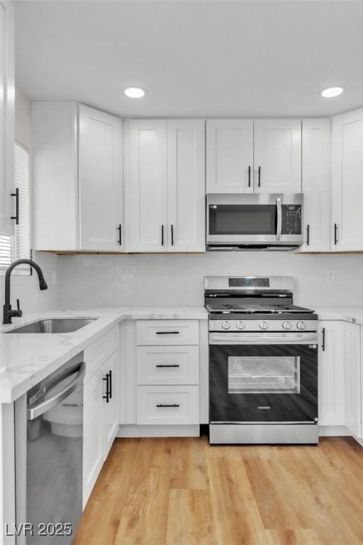 kitchen with light stone counters, a sink, white cabinetry, light wood-style floors, and appliances with stainless steel finishes