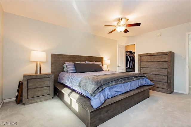 carpeted bedroom with a closet, a walk in closet, a ceiling fan, and baseboards