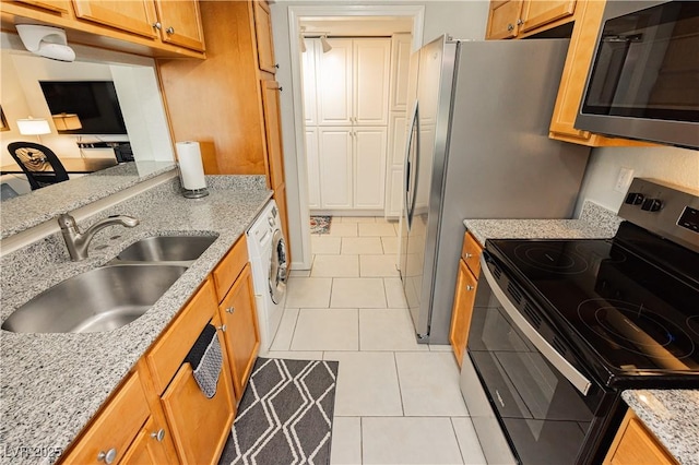 kitchen featuring light tile patterned floors, light stone counters, stainless steel appliances, a sink, and brown cabinetry