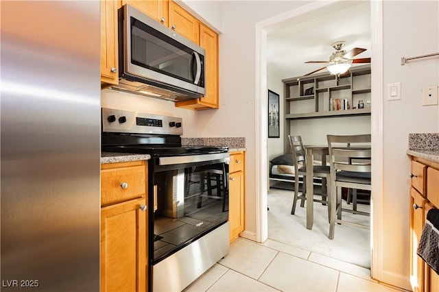 kitchen with light tile patterned floors, stainless steel appliances, light stone counters, and a ceiling fan