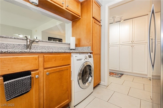 laundry area with cabinet space, light tile patterned floors, washer / clothes dryer, and a sink