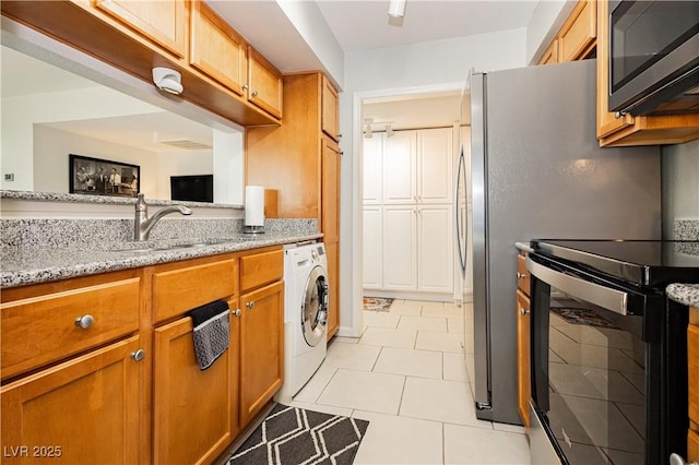 kitchen featuring black electric range, washer / clothes dryer, stainless steel microwave, a sink, and light stone countertops