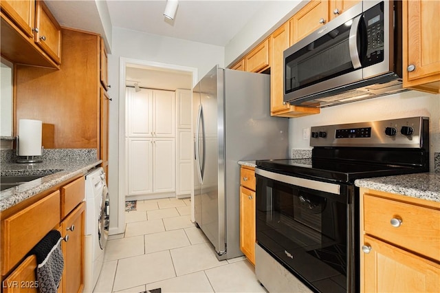 kitchen featuring appliances with stainless steel finishes, washer / clothes dryer, light stone counters, and light tile patterned floors