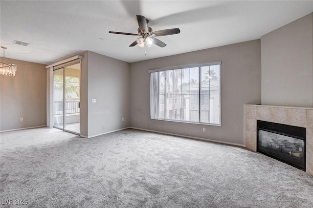 unfurnished living room with baseboards, visible vents, a tile fireplace, carpet floors, and ceiling fan with notable chandelier