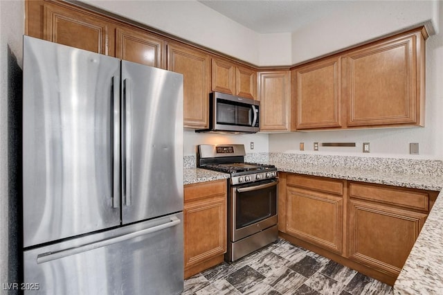 kitchen with appliances with stainless steel finishes, brown cabinets, and light stone counters