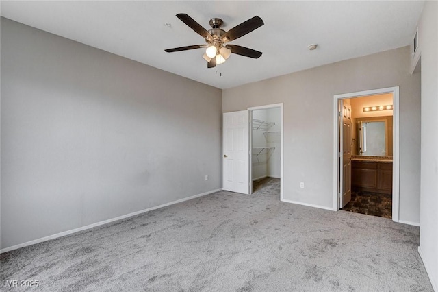 unfurnished bedroom featuring baseboards, ceiling fan, ensuite bath, a walk in closet, and carpet flooring