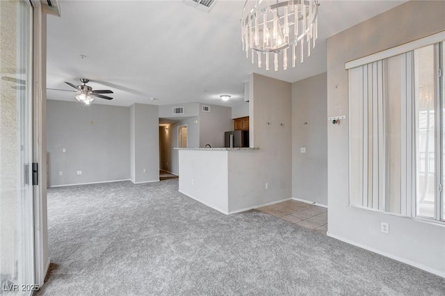 unfurnished living room featuring tile patterned flooring, ceiling fan with notable chandelier, carpet floors, visible vents, and baseboards