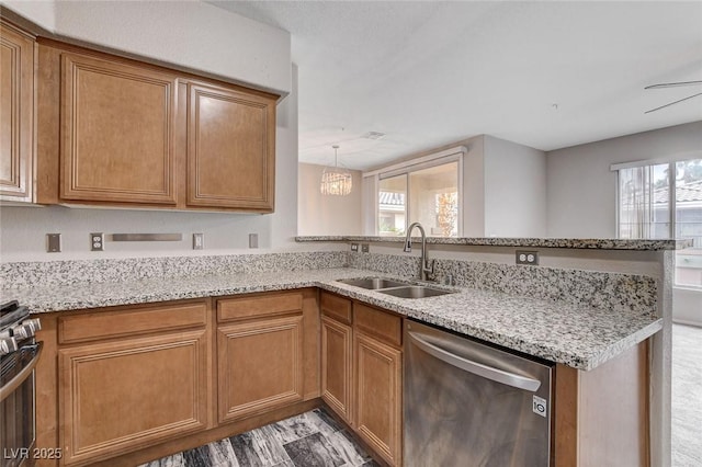 kitchen featuring brown cabinets, appliances with stainless steel finishes, a sink, light stone countertops, and a peninsula