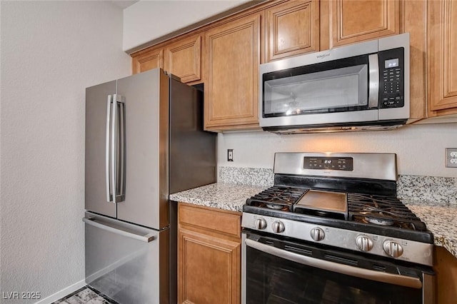 kitchen with appliances with stainless steel finishes, brown cabinetry, baseboards, and light stone counters