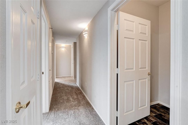 hallway featuring dark carpet and baseboards