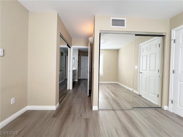 unfurnished bedroom with baseboards, a closet, visible vents, and wood finished floors