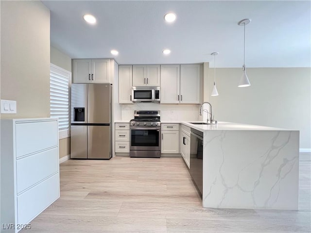 kitchen with light stone counters, a peninsula, a sink, hanging light fixtures, and appliances with stainless steel finishes