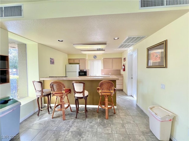 kitchen with black microwave, visible vents, a breakfast bar, and freestanding refrigerator