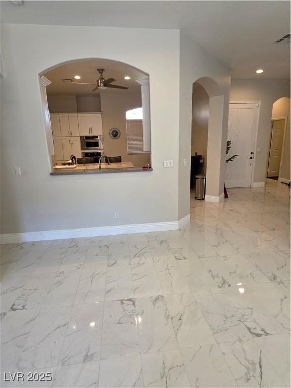 unfurnished living room featuring a ceiling fan, arched walkways, baseboards, and marble finish floor